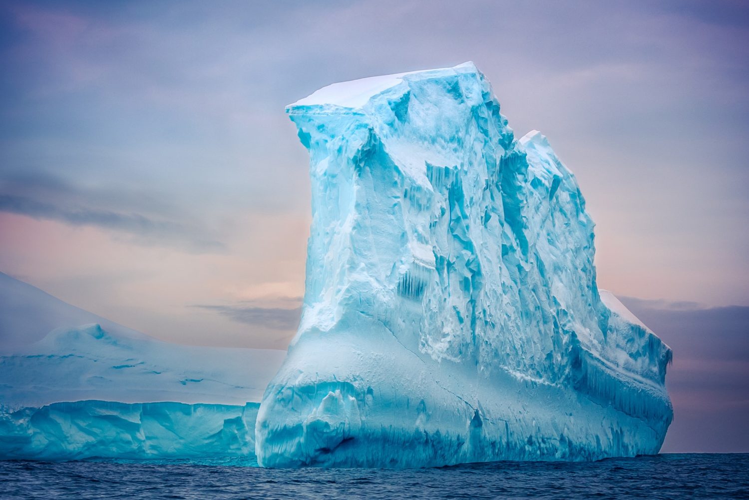 Antarctic iceberg of unusual form in the snow floating in open ocean. Pastel sunset sky in the background. Beauty world.