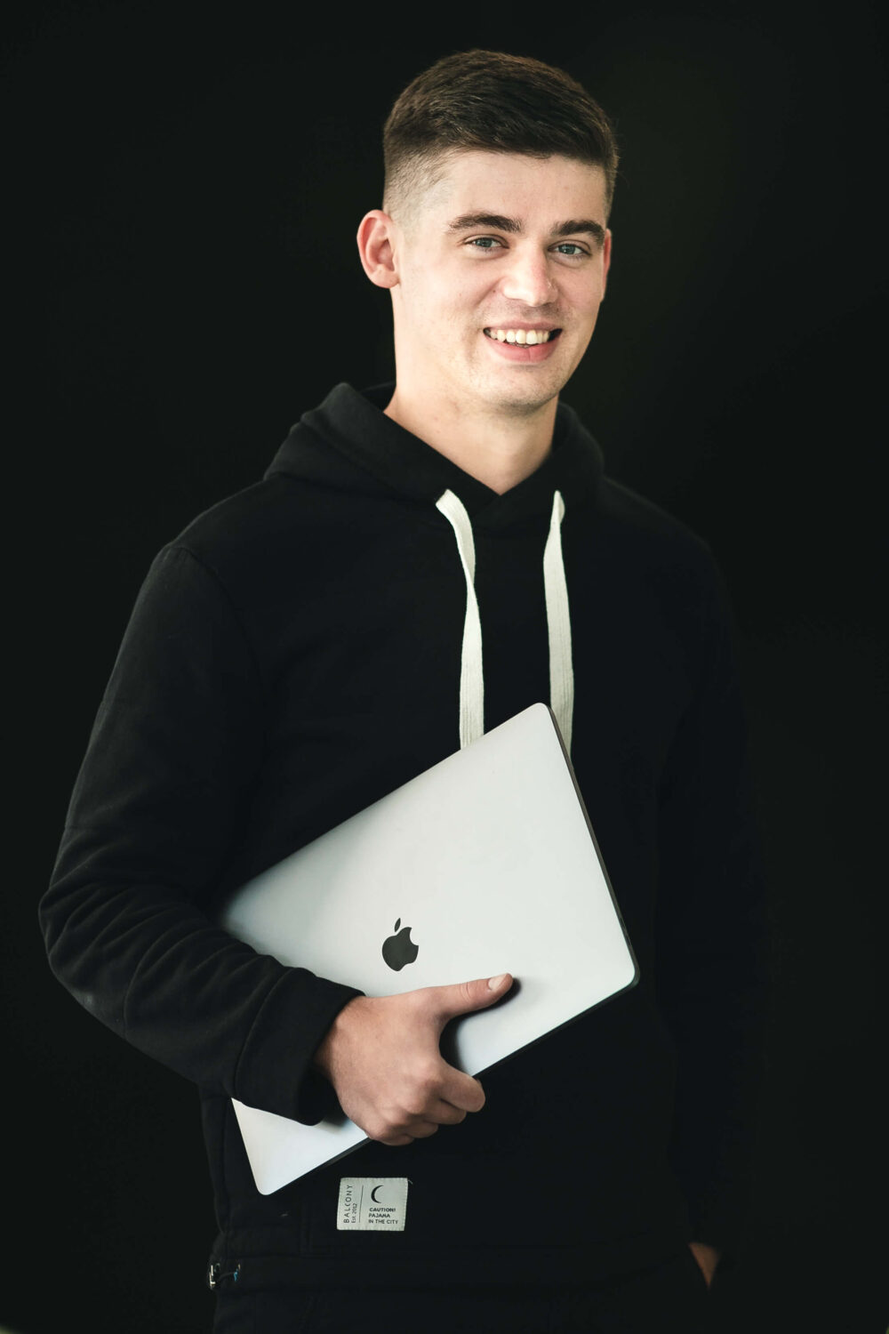 дизайнер Женя Шикірявий стоїть з ноутбуком у руках, одягнений у темний светр, усміхається